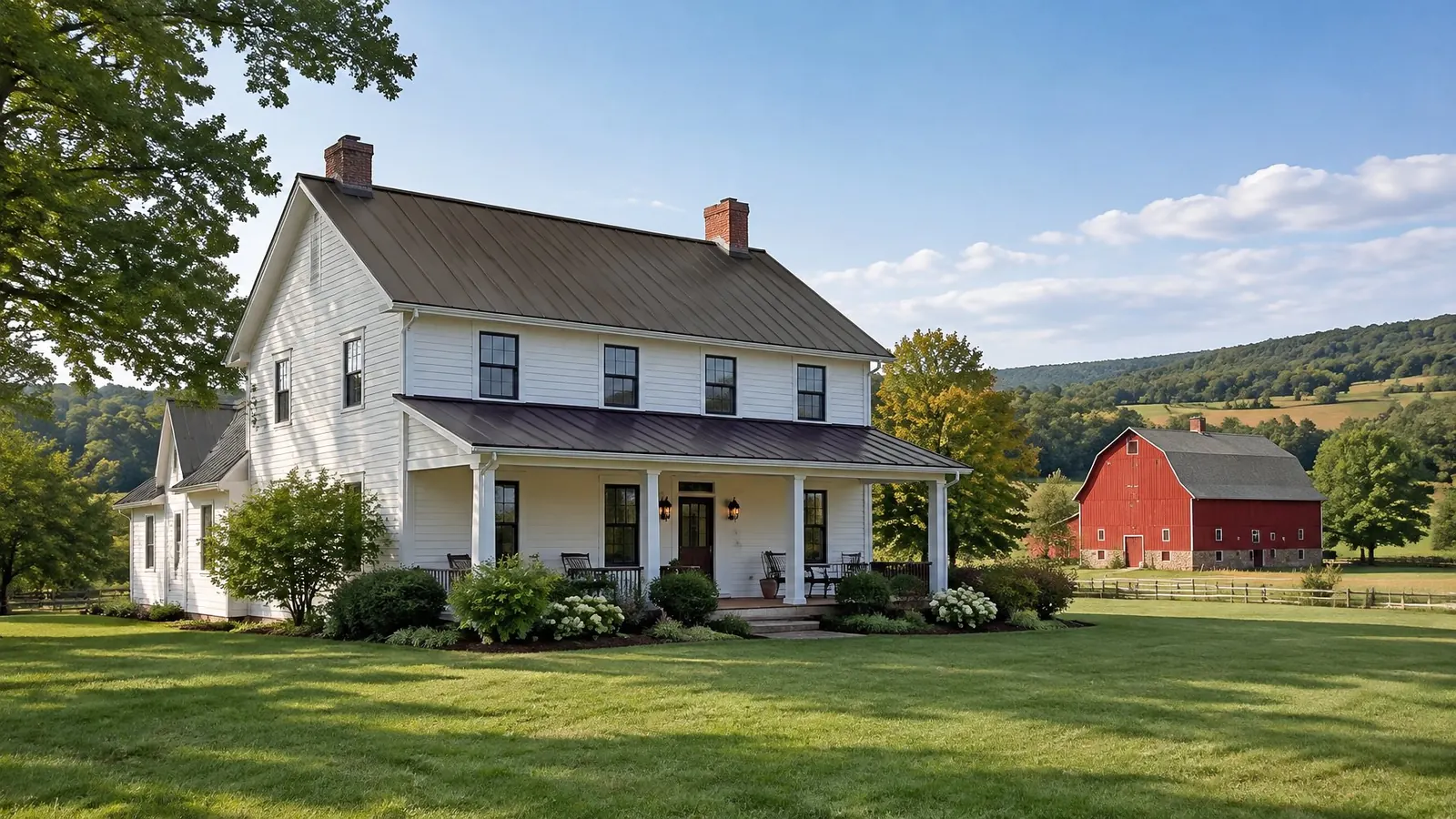Dark bronze standing seam metal roof on a white farmhouse with a deep porch, a red bank barn behind it