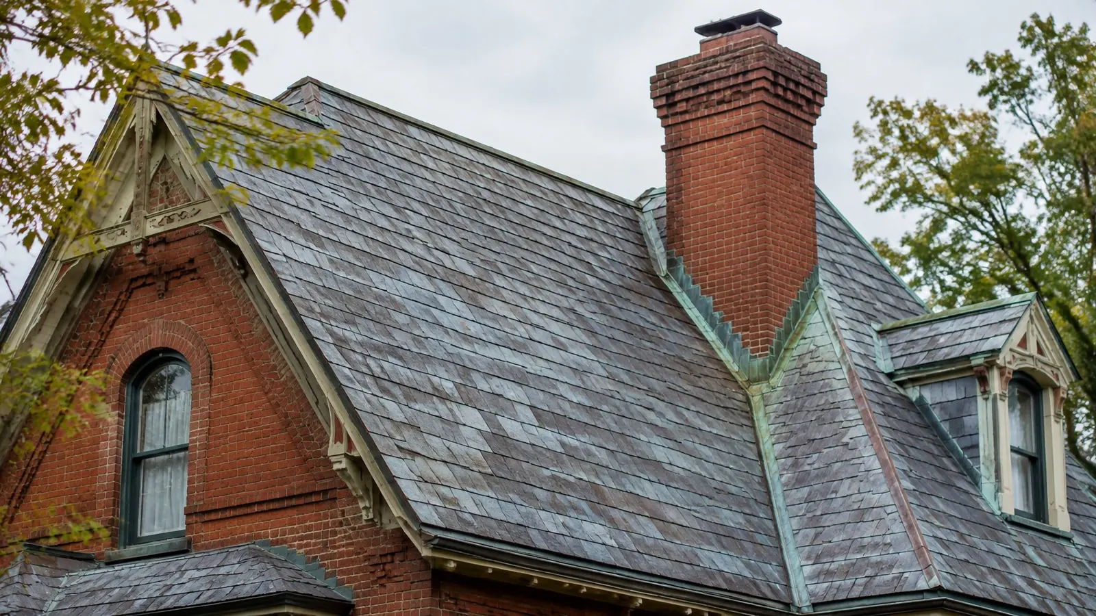 Weathered blue-gray slate roof with green copper valley flashing, a brick chimney and dormers on a Victorian brick house